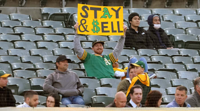 An Oakland Athletics fan holds up a sign urging team owner John Fisher to “stay and sell”